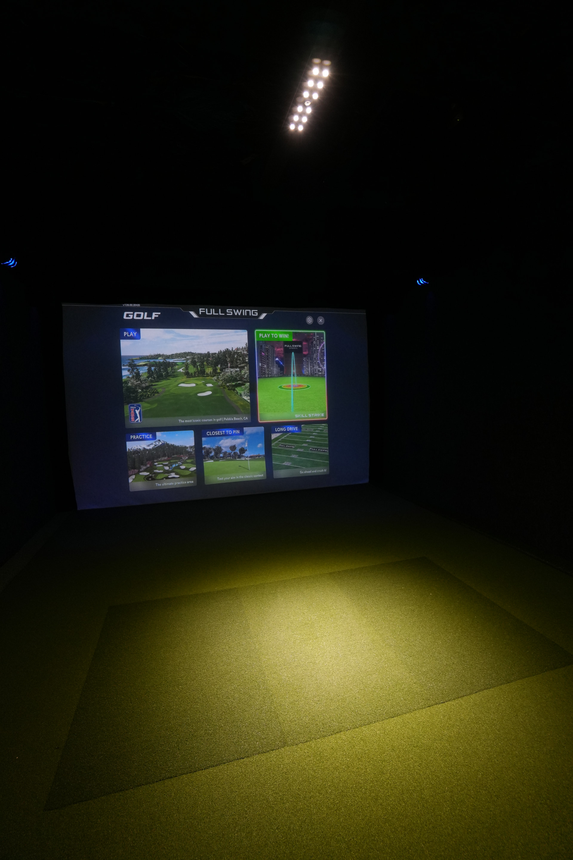 Inside a Back Nine Golf simulator bay. Yellow turf and a Full Swing screen.